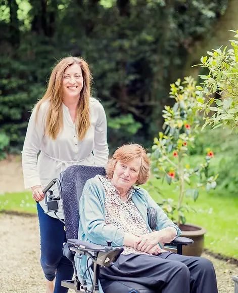 Eldery lady with companion care sat in pretty garden drinking cup of tea