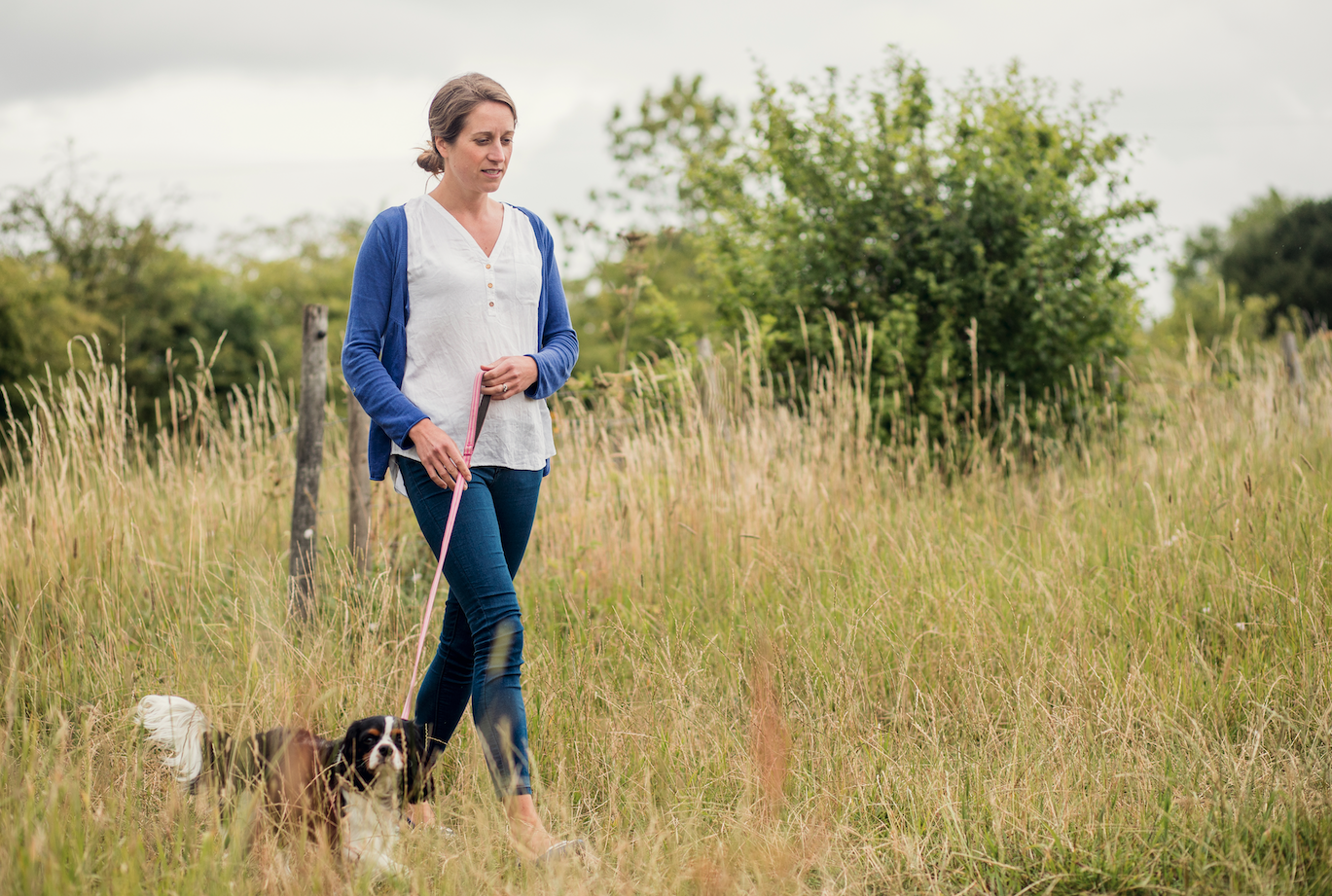 Home carer walking dog in a field in the country