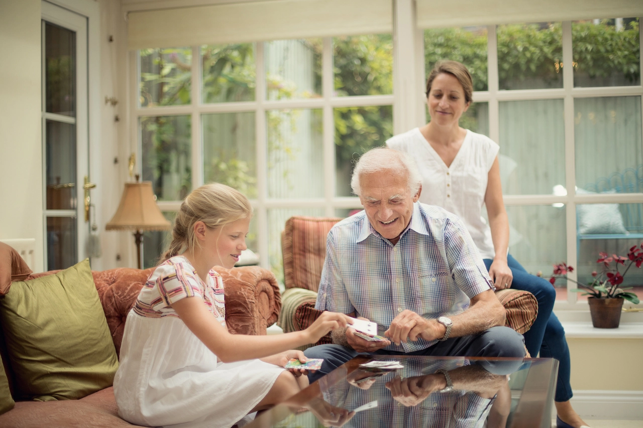 Elderly gentleman palying game with grandaughter at home with with home carer