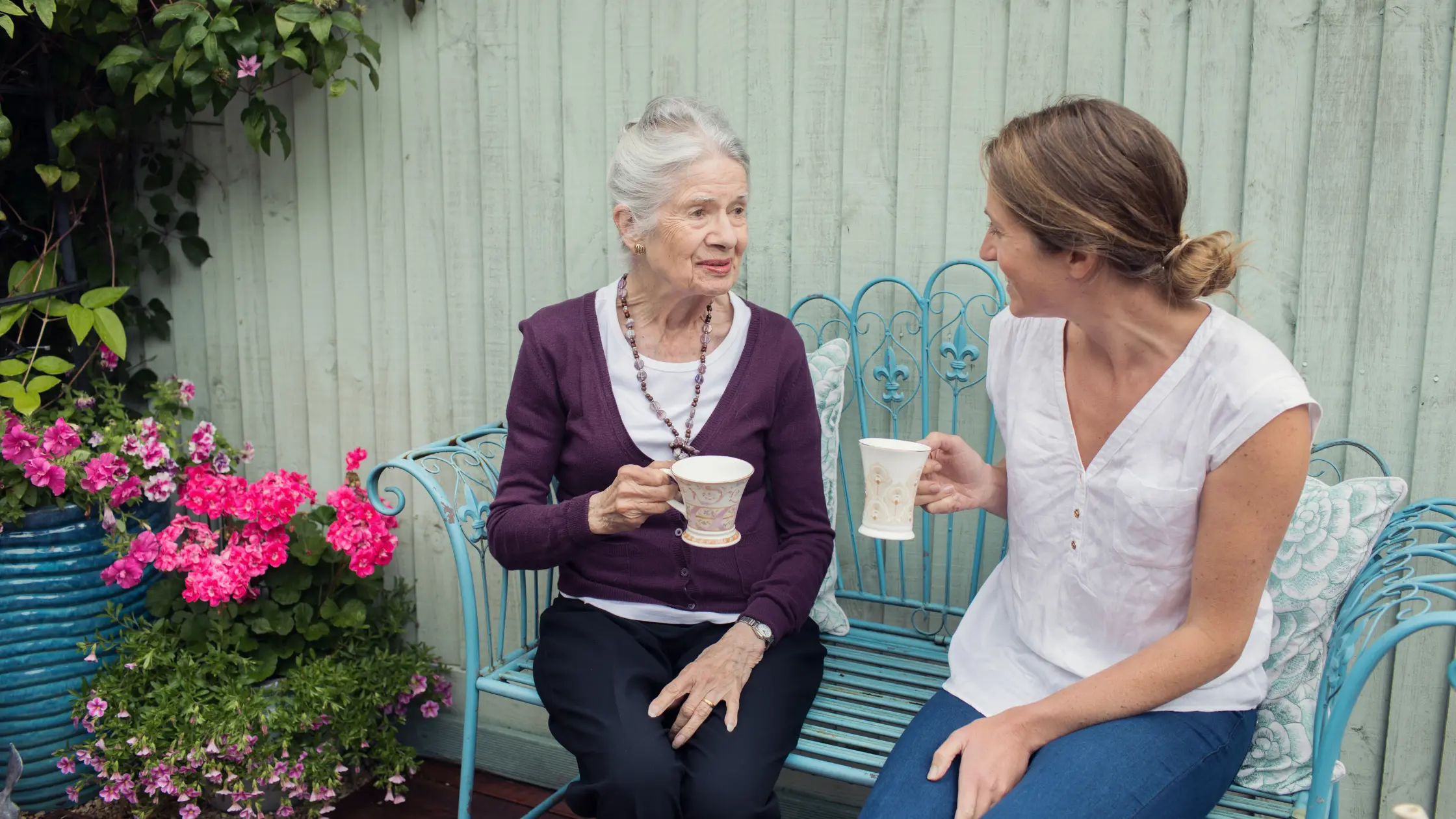 Elderly lady sat in garden with home carer drinking cup of tea