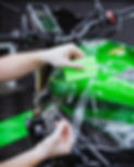 A Lux Lab installer expertly applying 3M Paint Protection Film (PPF) with a squeegee to the fuel tank of a green Kawasaki motorbike in Exeter.