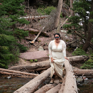 bride hikes through river bed balancing on logs glacier national park