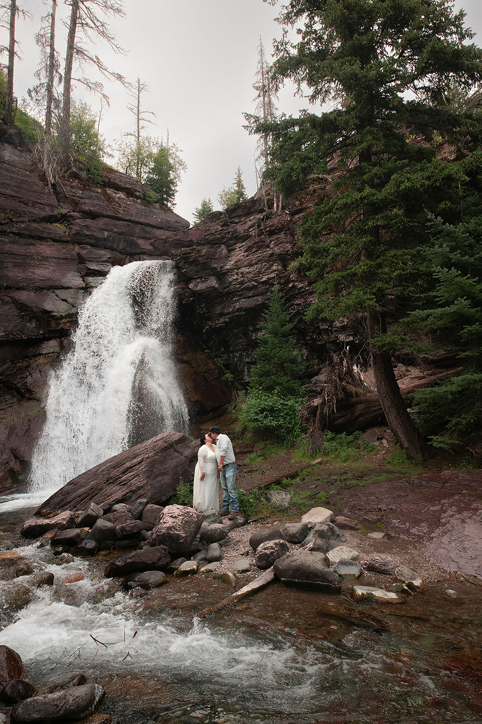 bride and groom kiss under barings falls summer glacier national park
