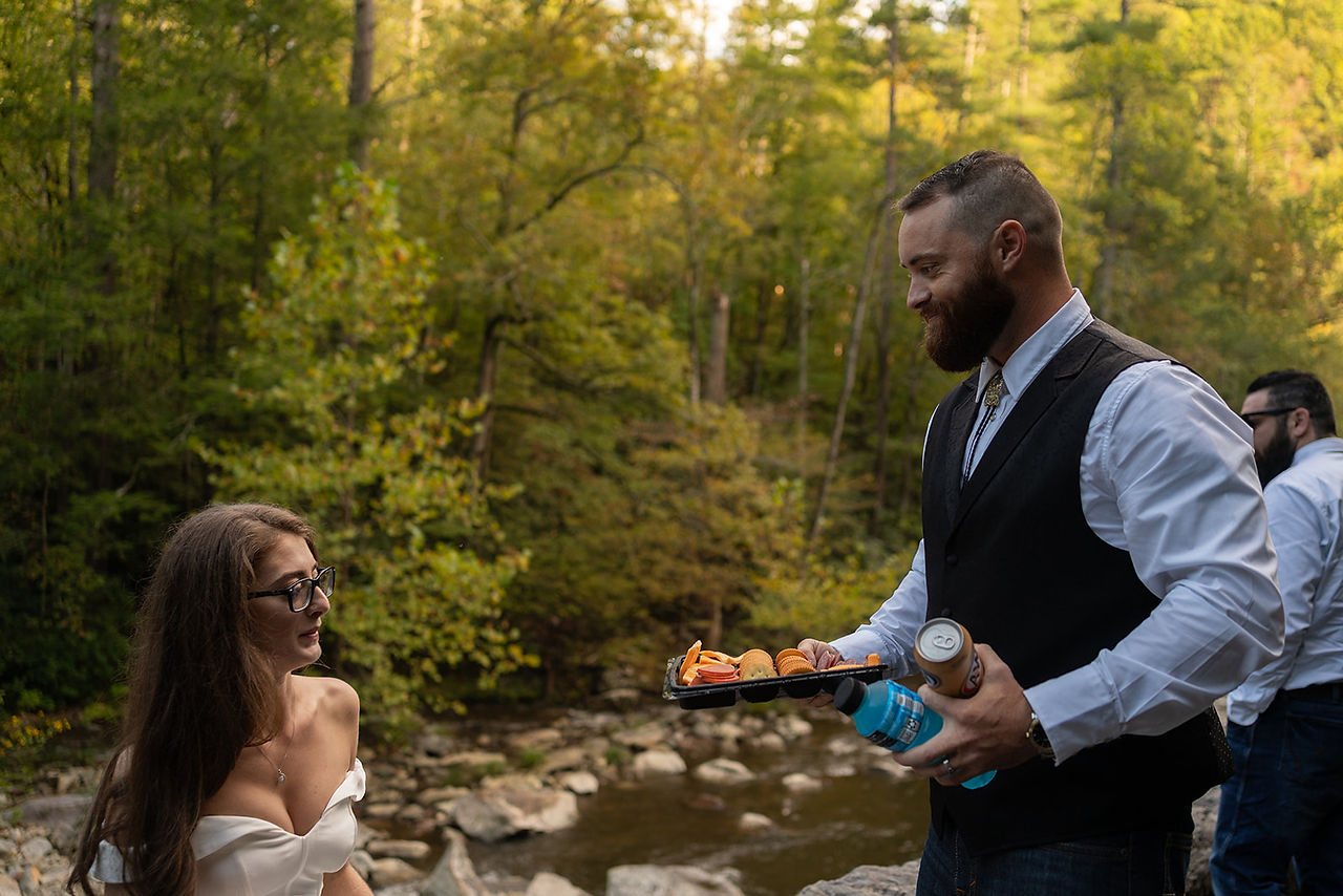 groom brings his bride a charcuterie plate for elopement picnic