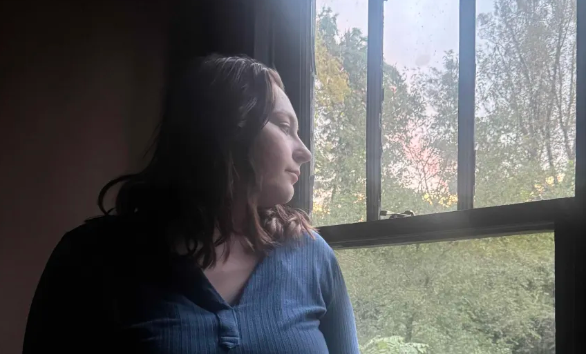 Emily Ammer stands by the window of her home on Friday, Sep. 19th, 2025, pondering if she should go out and trim some of the hedges in her backyard.