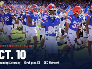 Florida players in blue jerseys and orange helmets run onto the field in afternoon sun at the Swamp, with pyro flames and smoke behind the band, during the Ole Miss game on Sept. 26, 2026. Photo by Chris Spears, GatorBait Media.