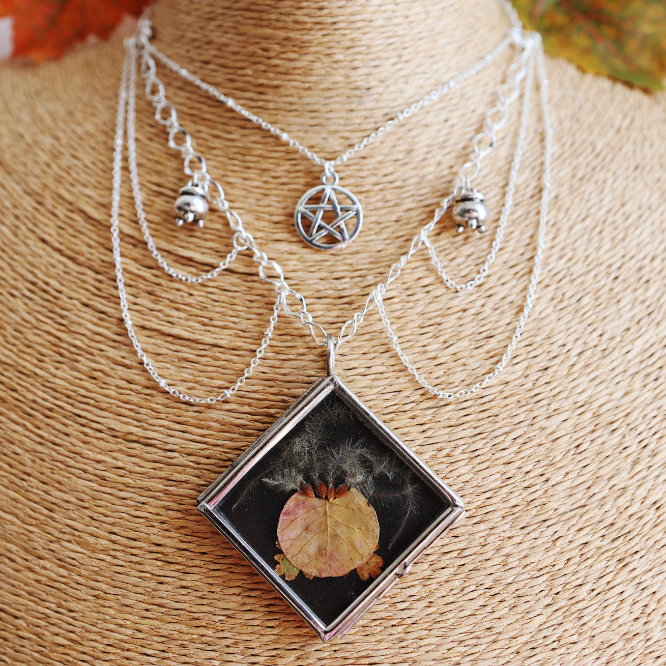a plastron necklace with a glass pendant holding plants representing a bubbling cauldron, a pentagram and cauldrons charms