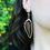 Miniature : A stained glass earring showcasing a real fern worn by a woman. We can see a flowery garden in the background