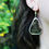 Miniature : A stained glass earring showcasing a real ivy leaf worn by a woman. We can see a flowery garden in the background