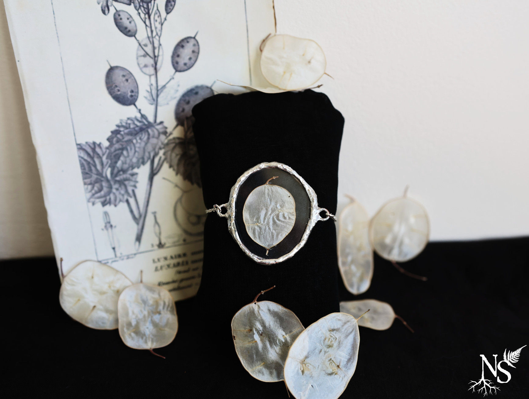 A stained glass bracelet showcasing a real pressed lunaria disc displayed on a black muff with lunaria decor around
