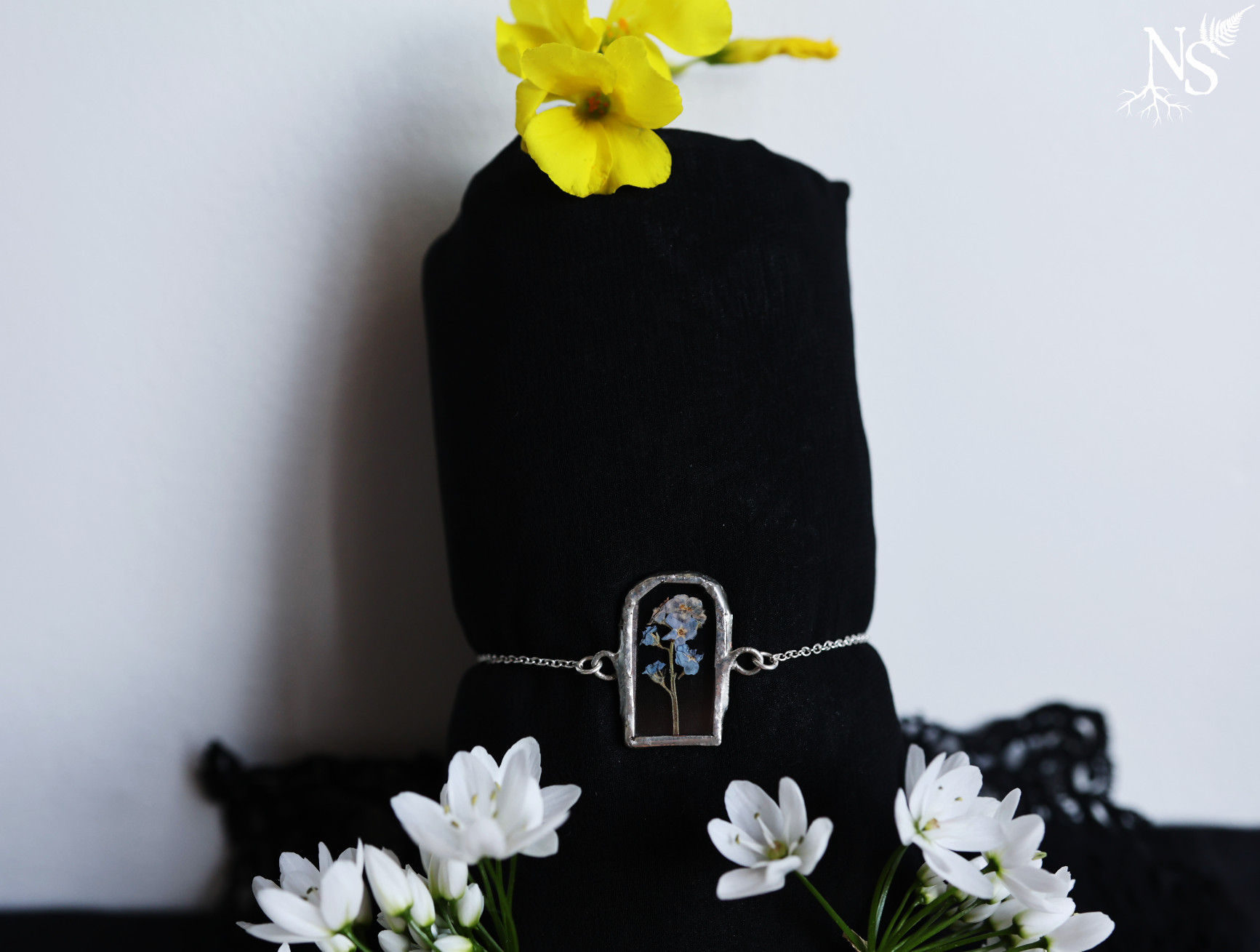 A stained glass bracelet showcasing a real flower displayed on a black muff with real flowers around