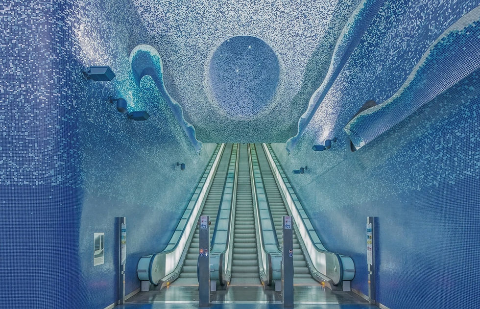 Blue-tiled subway escalator under a mosaic ceiling with a circular design. The setting is futuristic and tranquil, with no people visible.