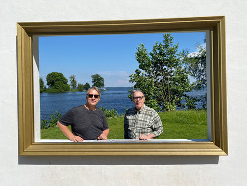 Kevin & Michael standing in a picture frame with a view of the lake behind them