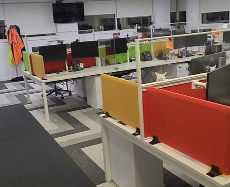 A bull-pen style office setup, complete with yellow, red, and green cubicle dividers and multiple monitors dotted around.