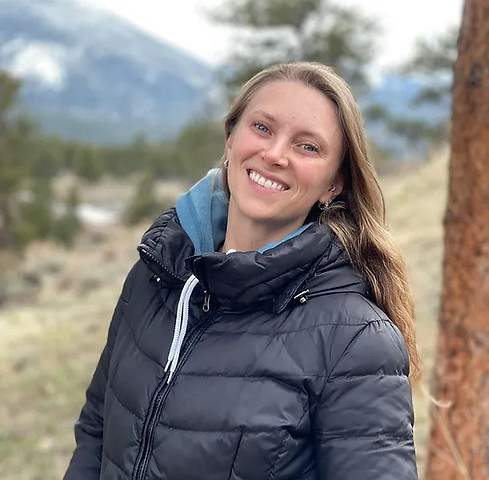 Uma mulher adulta sorrindo, com um fundo de montanhas e natureza.