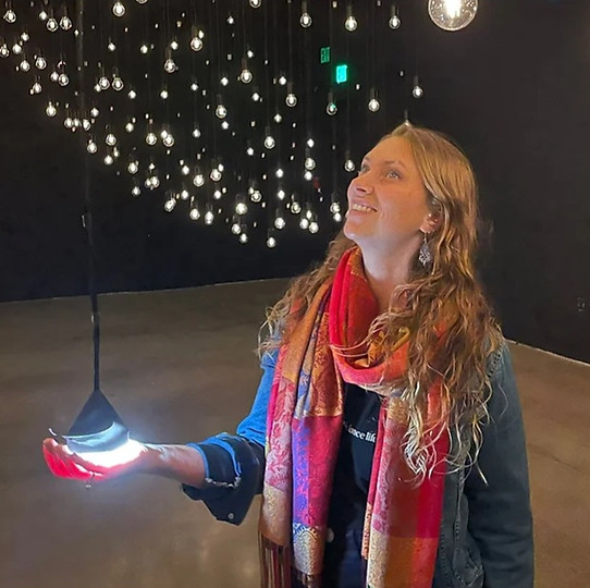 Uma mulher encostando a mão em um bulbo de uma lâmpada pendurada por um longo fio.