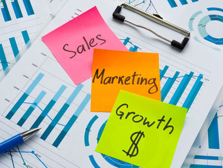 A pile of papers covered with graphs. On them has been placed sticky notes, a pink one with sales written on it, an orange one with marketing written on it, and a green one that says growth.