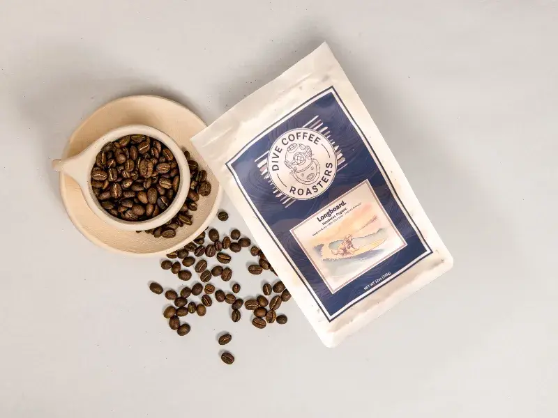 Longboard Coffee next to a Cup Full of Coffee Beans