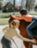 Woman helping girl mount a horse