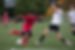 A photo of a high school-aged Issaquah FC boy about to kick a soccer ball during a game, with an opposing team player trying to defend, and other boys looking on.