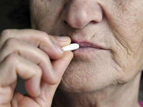 Elderly person holding a white pill near lips, preparing to take it. Focus on face and hand, highlighting skin texture. Somber mood.