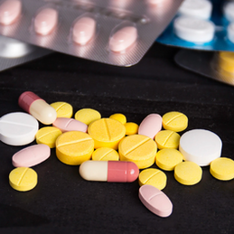 Various colorful pills and capsules scattered on a dark surface, with blister packs in the background.