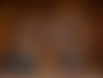 A straight on view of a deeply textured warm rust colored pegboard wall creatively displaying a curated variety of artisan chairs and stools. The top two rows appear to float against the rich brown background featuring smooth curved light oak frames matte black painted seats woven rattan stools and folded leather camp frames. Resting on the matching floor below is a neat arrangement of seating including a stacked set of black cane dining chairs alongside elegant wooden armchairs with soft grey fabric cushions.