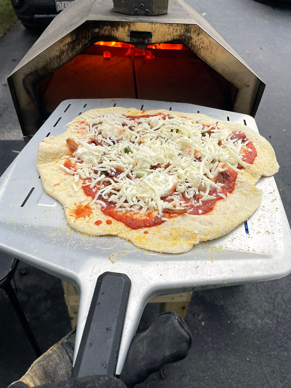 Pizza on a peel ready to enter a hot oven, glowing with embers. Topped with cheese and tomato sauce. Gray surface background.