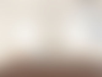 Serene hotel bedroom with neutral color palette, showing a bed dressed in a taupe channel-quilted comforter with white pillows and rolled towels arranged on top, flanked by wooden nightstands with modern white table lamps, white walls, and a mini-split air conditioner mounted above