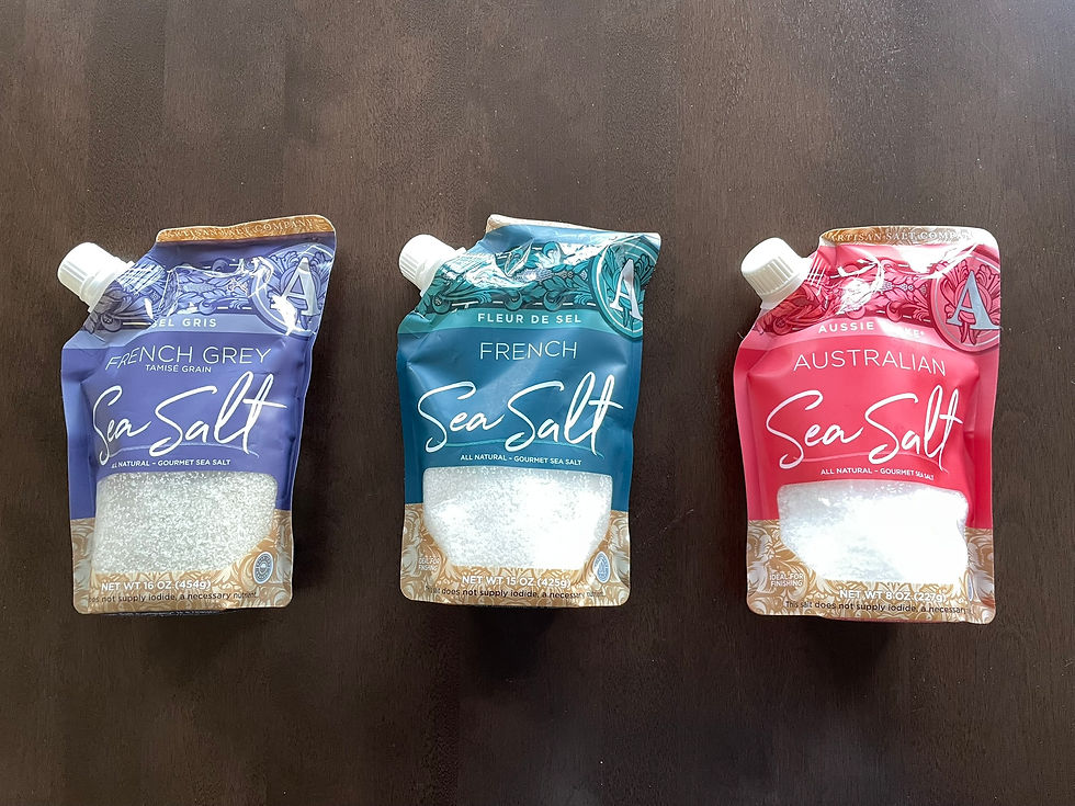 Three colorful pouches of sea salt on a dark wood table: French Grey (purple), French (blue), and Australian (red) with decorative designs.