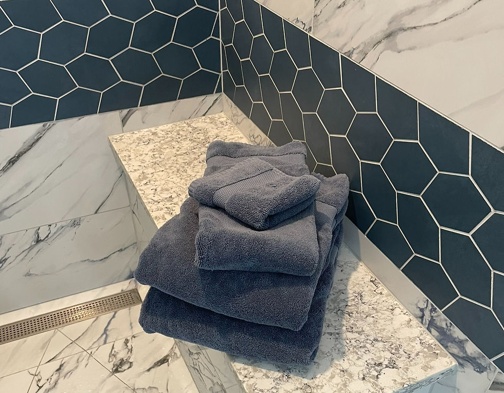 Folded blue towels on a marble bench in a bathroom with hexagonal blue and gray tiles. Clean, modern aesthetic.