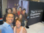 Steve and Mary Beth sharing a warm, nostalgic smile in the bright lights of The F.R.I.E.N.D.S Experience in Boston, standing before a large, vivid backdrop featuring the classic cast.