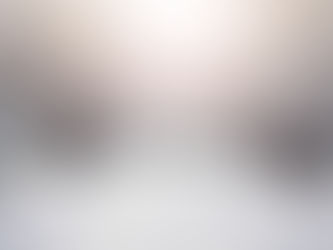 A serene winter landscape showing a wide snow-covered path or road stretching into the distance, flanked on both sides by mature trees heavily laden with snow and ice. The frost-covered branches create a natural canopy overhead, while soft, diffused light glows through the misty atmosphere, creating an ethereal tunnel effect. The scene conveys quiet, pristine winter beauty.