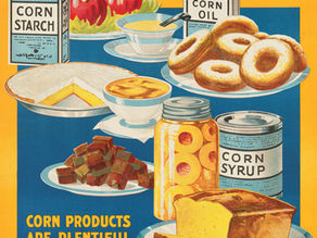 A colorful vintage food poster from the United States Food Administration titled 'Wholesome - Nutritious Foods from Corn' with an orange and blue color scheme. The poster displays various corn-based products including boxes of corn starch and corn oil, donuts on a plate, what appears to be cornbread or cake slices, candies, a jar of corn syrup, and other baked goods. Text at the bottom reads 'Corn Products Are Plentiful - Use Them In Cakes, Candies, Puddings and Preserving For Salads, Shortening and for Frying' followed by 'United States Food Administration.