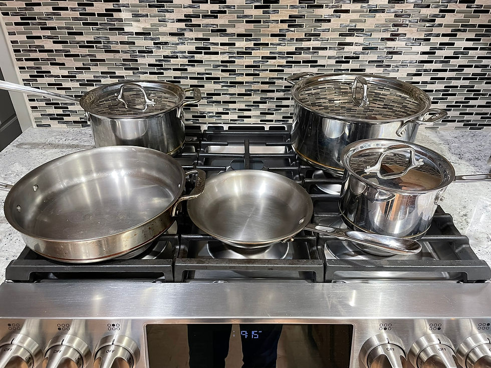 All-Clad stainless steel pots and pans on a stove with black and gray tile backsplash; oven display shows 9:51, creating a modern kitchen vibe.