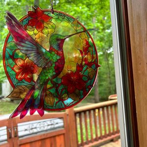 Stained glass hummingbird with red flowers; deck and outdoor view in background.