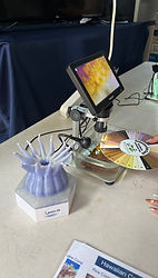 Close-up of a digital microscope screen displaying a detailed texture of coral, with a 3D-printed blue coral polyp model on the left and a color-coded Hawaiian Koʻa assessment card on the right.