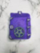 Bath bomb in the shape of a purple spell book with green and silver details