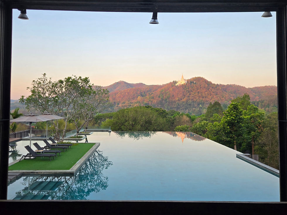 Infinity pool with lounge chairs under umbrellas overlooks lush hills and a distant temple at sunset. Tranquil and serene atmosphere.