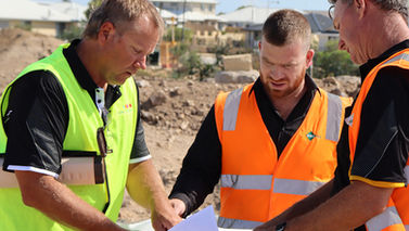 Three men wearing hi-vis looking over town plans.