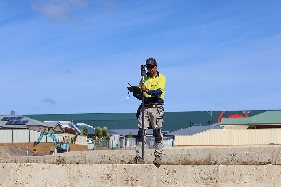 Surveyor in high-vis gear uses equipment on a construction site. Blue sky, buildings, and excavator in the background. Calm mood.