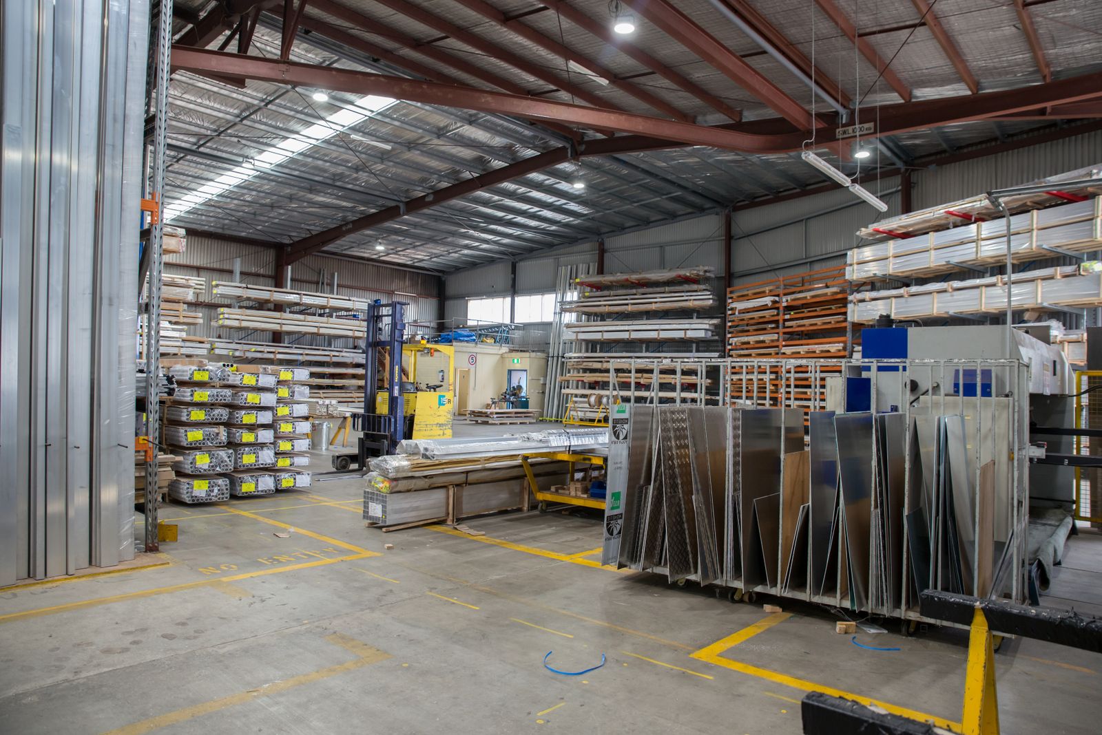 Warehouse interior with stacked metal sheets, racking and marked floor lanes
