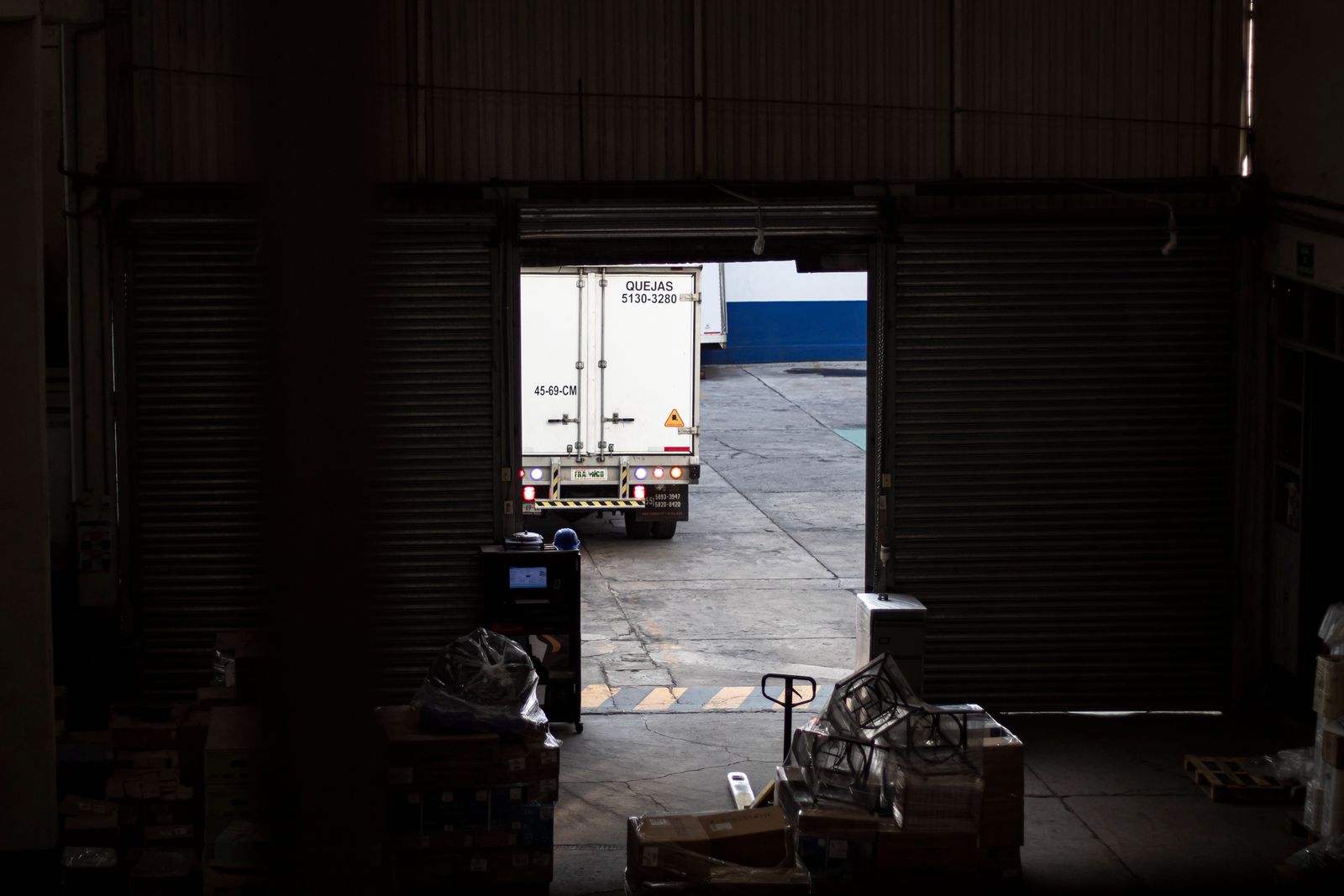 Delivery truck leaving a dimly lit warehouse loading dock with pallets and parcels inside