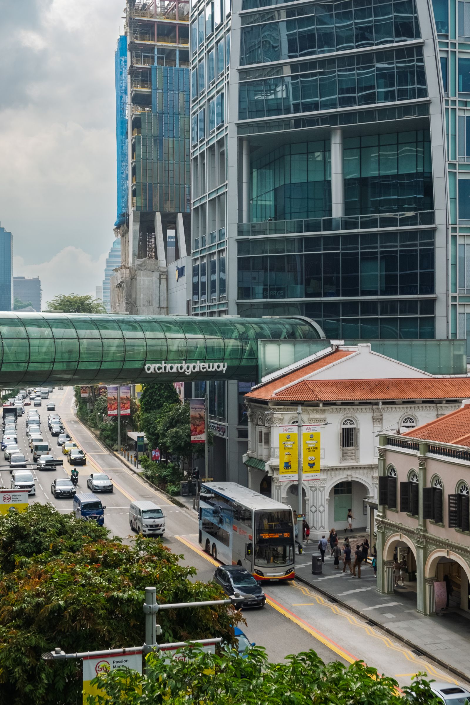 Traffic on Orchard Road beneath a glass link bridge, with conserved shophouses beside the road