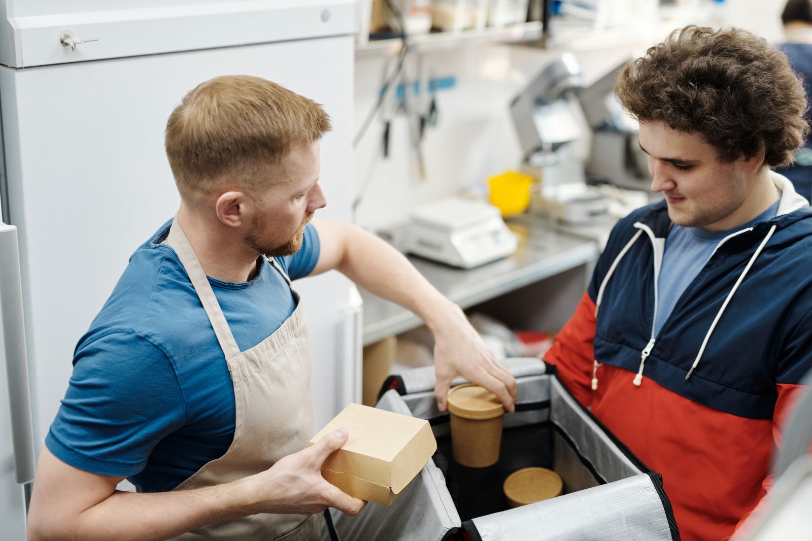 Two kitchen staff packing food containers into bags for delivery orders