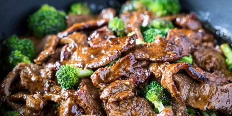 Close-up of beef and broccoli stir-fry, glistening with sauce. Vibrant green broccoli contrasts with the rich brown beef in a pan.