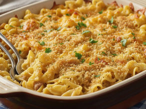 Baked macaroni and cheese in a rectangular dish with a golden breadcrumb topping, garnished with parsley. A spoon and fork are on the side.