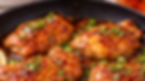 Chicken thighs glazed with a glossy orange sauce in a skillet, garnished with fresh herbs and green onions, create a savory and appetizing mood.