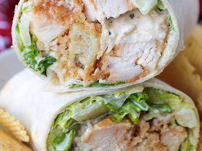 Close-up of a chicken Caesar wrap with crispy lettuce, croutons, and creamy dressing. Served on a plate with ridged potato chips.