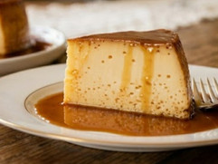 Slice of Venezuelan quesillo topped with golden caramel sauce, served on a white plate with a rich, creamy texture and rustic dessert presentation.